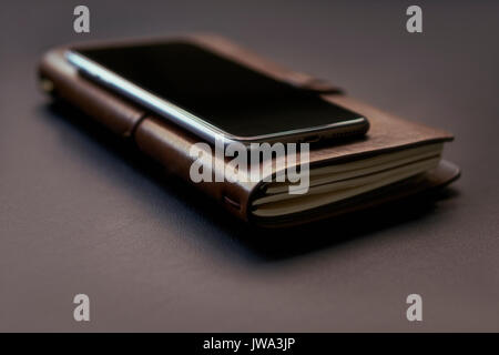 Closeup ist das Telefon in der Brieftasche ist aus Leder auf Ihrem Desktop. Der Bildschirm zeigt die Reflexion von Sonnenlicht aus dem Fenster. Stockfoto