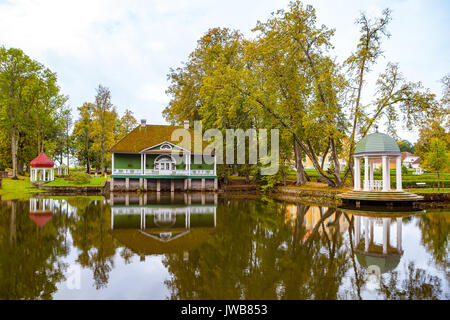 Blick auf einen Teich und grünes Holzhaus und zwei Pavillons mit Spiegelung im Wasser. Palmse Manor, Estland Stockfoto