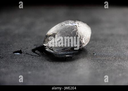 Ein Stück Eis, der gerade begann, liegt auf einer schwarzen Oberfläche zu schmelzen. Stockfoto