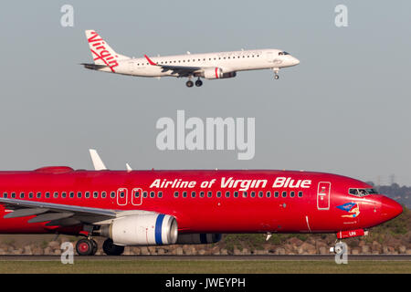 Pacific Blue Airlines (Jungfrau Australien Airlines) Boeing 737 auf der Landebahn am Flughafen Sydney mit einer Jungfrau Embraer E-190 Landung hinter sich. Stockfoto