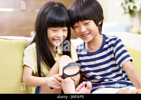 Zwei asiatische Kinder sitzen auf der Couch zu Hause Spaß spielen mit einer Lupe. Stockfoto