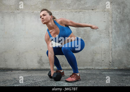 Mädchen wirft eine Hantel in eine Schulung in der Nähe einer Betonwand Stockfoto