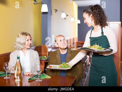 Lächelnde junge Kellnerin Älteres Paar beim Abendessen im Cafe mit Stockfoto