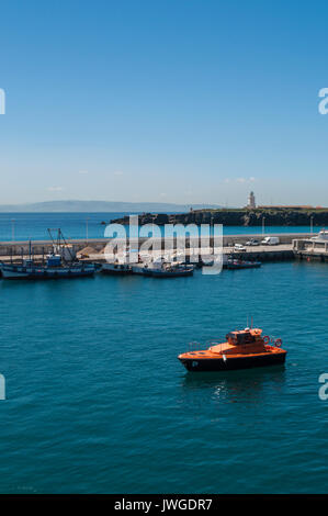 Ein Schiff in den Hafen von Tarifa, mit Blick auf die Meerenge von Gibraltar und Marokko, mit dem der Leuchtturm von Punta de Tarifa (Tarifa) im Hintergrund Stockfoto