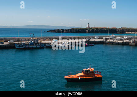 Ein Schiff in den Hafen von Tarifa, mit Blick auf die Meerenge von Gibraltar und Marokko, mit dem der Leuchtturm von Punta de Tarifa (Tarifa) im Hintergrund Stockfoto