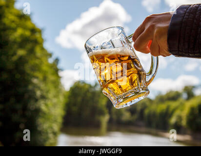 Weibliche hand mit einem Becher Bier in der Nähe des Sees an einem sonnigen Sommertag Stockfoto