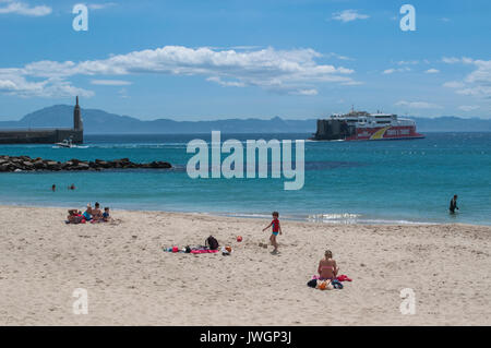 Menschen am Playa Chica, Strand am Ende der Hafen von Tarifa mit Blick auf die Straße von Gibraltar und Marokko, mit der Statue Sagrado Corazon de Jesus Stockfoto