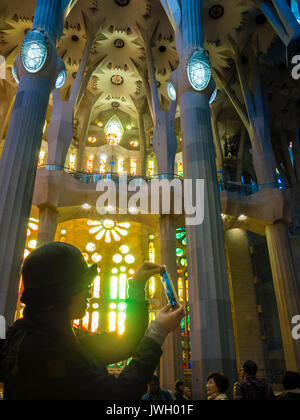 Eine asiatische Tourist ist das Aufnehmen von Fotos mit einem Smartphone innerhalb Barcelonas Kathedrale Sagrada Familia, die mit Besuchern aus der ganzen wor voll ist Stockfoto