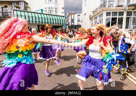 Jährliche Broadstairs Folk Woche Festival. Volkstänzer, Lose Frauen Morris Seite tanzen auf der Straße und halten Holz hell farbigen Pole. Tragen rainbow tatter Jacken. Stockfoto