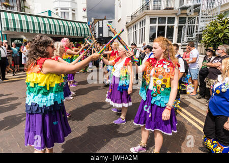 Jährliche Broadstairs Folk Woche Festival. Volkstänzer, Lose Frauen Morris Seite tanzen auf der Straße und halten Holz hell farbigen Pole. Tragen rainbow tatter Jacken. Stockfoto