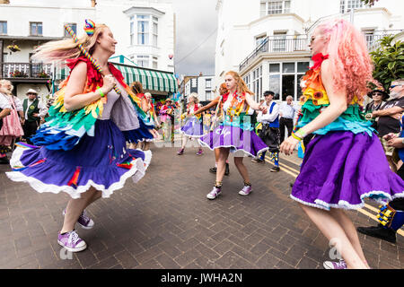 Jährliche Broadstairs Folk Woche Festival. Volkstänzer, Lose Frauen Morris Seite tanzen auf der Straße und halten Holz hell farbigen Pole. Tragen rainbow tatter Jacken. Stockfoto