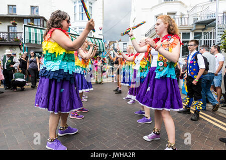 Jährliche Broadstairs Folk Woche Festival. Volkstänzer, Lose Frauen Morris Seite tanzen auf der Straße und halten Holz hell farbigen Pole. Tragen rainbow tatter Jacken. Stockfoto