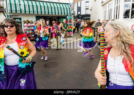 Jährliche Broadstairs Folk Woche Festival. Volkstänzer, Lose Frauen Morris Seite tanzen auf der Straße und halten Holz hell farbigen Pole. Tragen rainbow tatter Jacken. Stockfoto