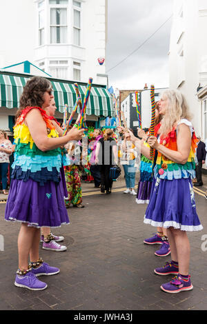 Jährliche Broadstairs Folk Woche Festival. Volkstänzer, Lose Frauen Morris Seite tanzen auf der Straße und halten Holz hell farbigen Pole. Tragen rainbow tatter Jacken. Stockfoto