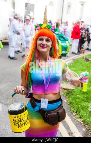Sehr glückliche junge Frau, 20s, das Tragen von Rainbow top und orange Haare. Bis bubble Aerosol blasen, und in der anderen Hand Sammlung Schaufel für die broadstairs Folk Woche Festival. Stellt für Bild, close-up. Auge - Vertrag. Stockfoto