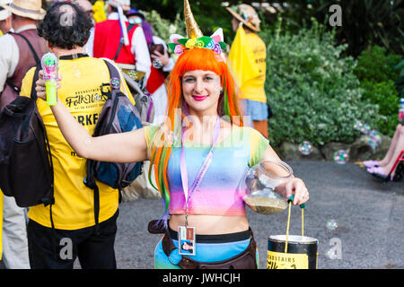 Sehr glückliche junge Frau, 20s, das Tragen von Rainbow top und orange Haare. Bis bubble Aerosol blasen, und in der anderen Hand Sammlung Schaufel für die broadstairs Folk Woche Festival. Stellt für Bild, close-up. Auge - Vertrag. Stockfoto