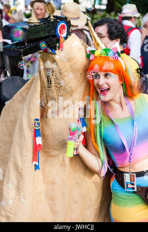 Sehr glückliche junge Frau, 20s, das Tragen von Rainbow top und orange Haare. Bis bubble Aerosol blasen, und in der anderen Hand Sammlung Schaufel für die broadstairs Folk Woche Festival. Posen mit Ossie, Symbol Vogel Symbol Kreatur. Close-up. Stockfoto