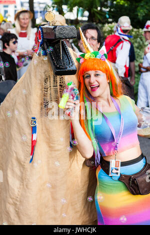 Sehr glückliche junge Frau, 20s, das Tragen von Rainbow top und orange Haare. Bis bubble Aerosol blasen, und in der anderen Hand Sammlung Schaufel für die broadstairs Folk Woche Festival. Posen mit Ossie, Symbol Vogel Symbol Kreatur. Close-up. Auge - Vertrag. Stockfoto