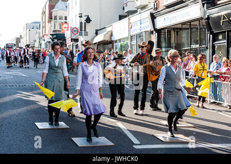 Broadstairs Folk Woche Festival Parade. Tippen Sie auf und Synchronisieren der Frauen Morris Dancers tanzen in der High Street, während Gelb schwenkten Taschentücher. Parade im Hintergrund, Leute beobachten auf Pflaster. Stockfoto