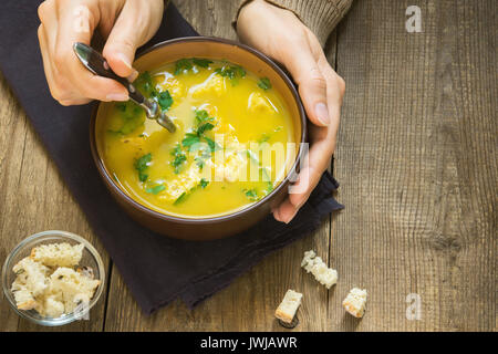 Frau Hände halten Schüssel Suppe mit Petersilie und Croutons über Holz- Hintergrund - gesunde winter Herbst vegetarische Kost Stockfoto