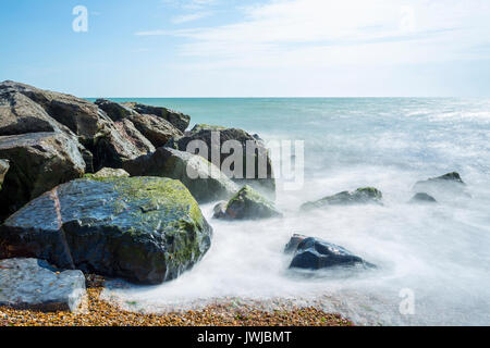 Wellen, die auf steinigen Strand und Felsen, mit blauem Himmel und Wolken. Avon Strand, Christchurch, Hampshire, Großbritannien Stockfoto