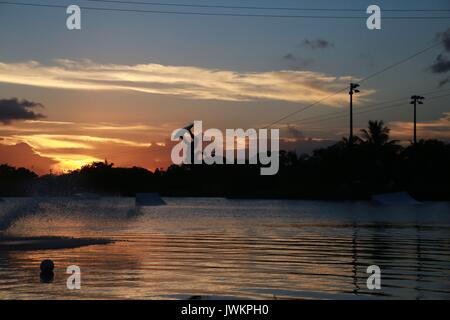 Wake Boarder auf der See bei Sonnenuntergang und hinter einer Wolke aus Wassernebel Stockfoto