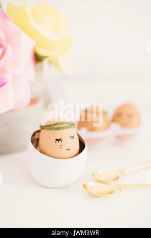 Ostern Konzept. Eier mit gemalten Augen und Mund. Ei Mädchen in Weiß. Blumen, Rosen Stockfoto