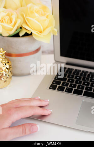 Feminine Workplace Konzept. Freier Arbeitsplatz mit Laptop, Blumen, goldene Ananas, Frau Hand. Blogger arbeiten. Hell, Gelb und Gold Stockfoto