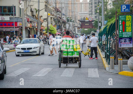 Ein Mann reitet ein Dreirad mit Kästen besteht, die entlang einem Büste Road in Shanghai, China, geladen. Stockfoto