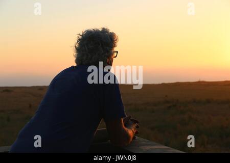 Älterer Mann sieht sie im Sonnenuntergang in einem Moment der friedlichen Einsamkeit. Stockfoto