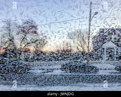 Eiskristalle eingefroren auf ein Auto Windschutzscheibe nach einem sub-zero Nacht im Winter mit dem Glanz der frühen Morgen Sonnenaufgang hinter einem Suburban House Stockfoto