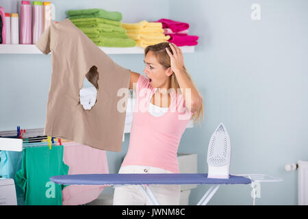 Junge Schockiert Frau mit Tuch in der Nähe der Verbrannten Bügeleisen Bügelbrett zu Hause stehend Stockfoto