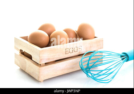 Eier in eine Holzkiste mit Blau ei Schneebesen auf weißem Hintergrund Stockfoto