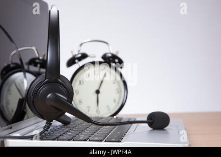 Laptop mit einem Headset auf der Tastatur und Wecker hinter closeup niedrigen Winkel über die Tasten mit Kopie Raum gesehen Öffnen Stockfoto