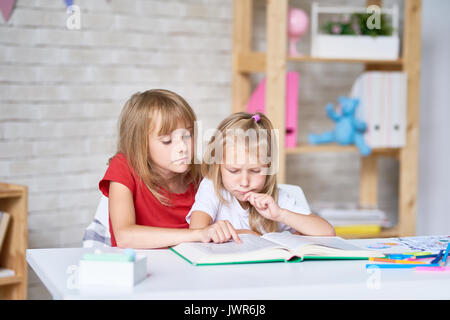 Adorable kleinen Schwestern eingehüllt in der Lesung Abenteuer Geschichte beim Sitzen am Tisch in Ihrem gemütlichen Schlafzimmer Stockfoto