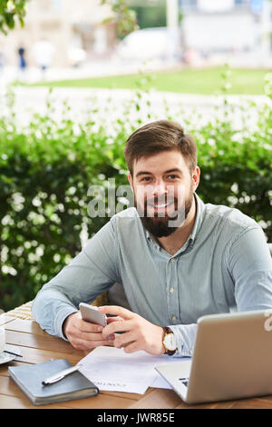 Portrait der junge Bartgeier Geschäftsmann auf Kamera und bei der Arbeit im Cafe im Freien lächeln Stockfoto