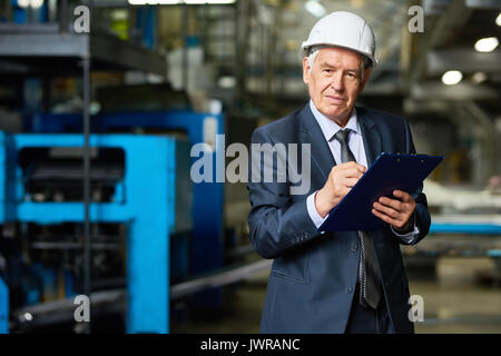 Portrait von älteren Geschäftsmann, tragen, hardhat an Kamera holding Zwischenablage in der Werkstatt der moderne Fabrik suchen Stockfoto