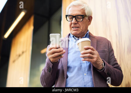 Portrait des modernen älterer Mann mit Smartphone im Freien, im Ort Straße holding Tasse Kaffee in der einen Hand Stockfoto
