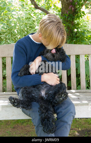 Eine blonde teenaged Jungen Umarmungen seiner schwarzen Hund Stockfoto