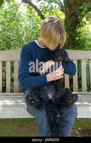 Eine blonde teenaged Jungen Umarmungen seiner schwarzen Hund Stockfoto