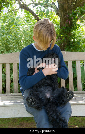 Eine blonde teenaged Jungen Umarmungen seiner schwarzen Hund Stockfoto