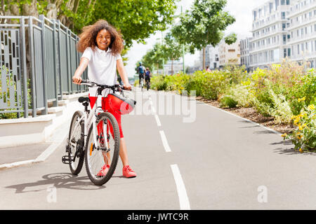 Full-length Portrait von Jugendlichen Afrikanische stehendes Mädchen mit ihrem Fahrrad auf dem Radweg im City Park Stockfoto