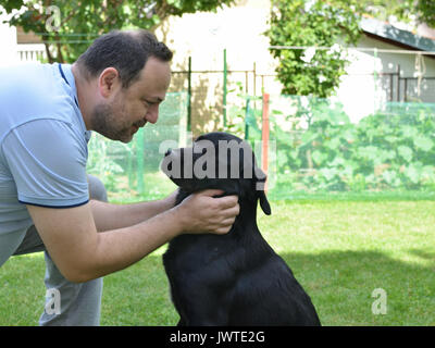Mann kuscheln und im Gespräch mit seinem besten Freund - Black Dog - in einem Garten Stockfoto