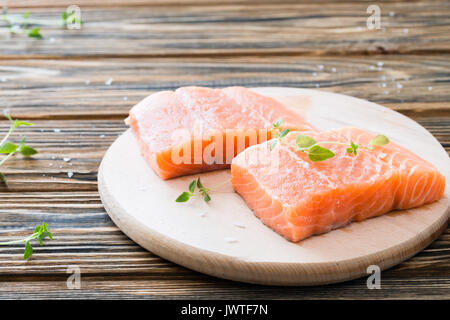 Zwei Stück Filet von der rohen ungekochten Lachs auf Schneidebrett garniert mit frischem Thymian auf hölzernen Tisch Stockfoto