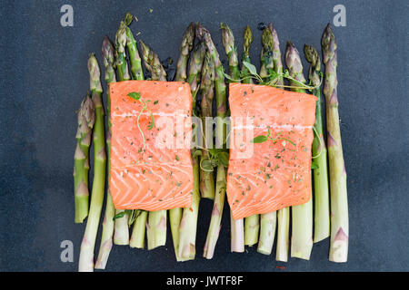 Zwei Stück Filet von der rohen ungekochten Lachs auf grünem Spargel auf Backblech garniert mit frischem Thymian. Zutaten für Mittag- oder Abendessen. Ansicht von oben Stockfoto