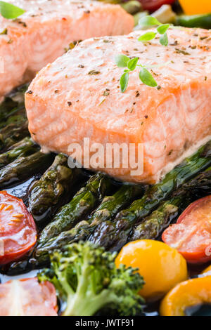 Zwei Stück Filet vom gebackenen Lachs auf grünem Spargel, Paprika, Tomaten und Brokkoli auf Backblech garniert mit frischem Thymian. Warmes Mittagessen Stockfoto