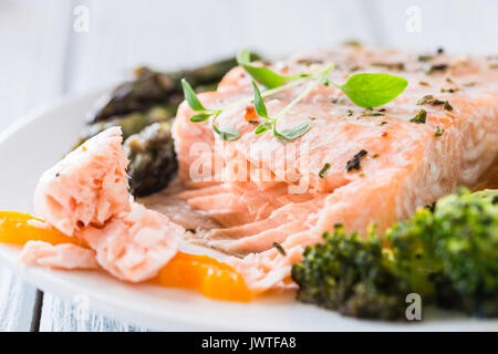 Gebackenes Lachsfilet mit Pfeffer, Spargel, Brokkoli und frischem Thymian auf weiße Platte serviert. Holztisch. Mittag- oder Abendessen. Nahaufnahme Stockfoto