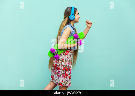 Hipster in motion auf hellblauem Hintergrund. Die jungen gerne schöne Langhaarige blonde Mädchen in Kleidung und Kopfhörer, Grün Kunststoff penny Ska Stockfoto