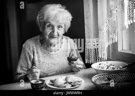 Ältere Frau isst am Tisch sitzen. Schwarz-weiß-Foto. Stockfoto