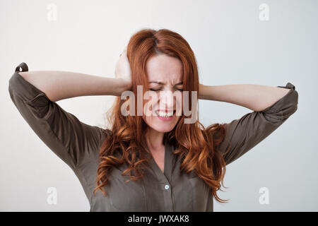 Langhaarige schöne junge brünette Frau für ihre Ohren mit den Händen Stockfoto